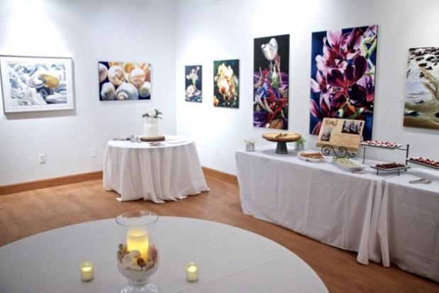 Tables with white tableclothes, candles, and table decorations, catered food, various paintings on the wall. 